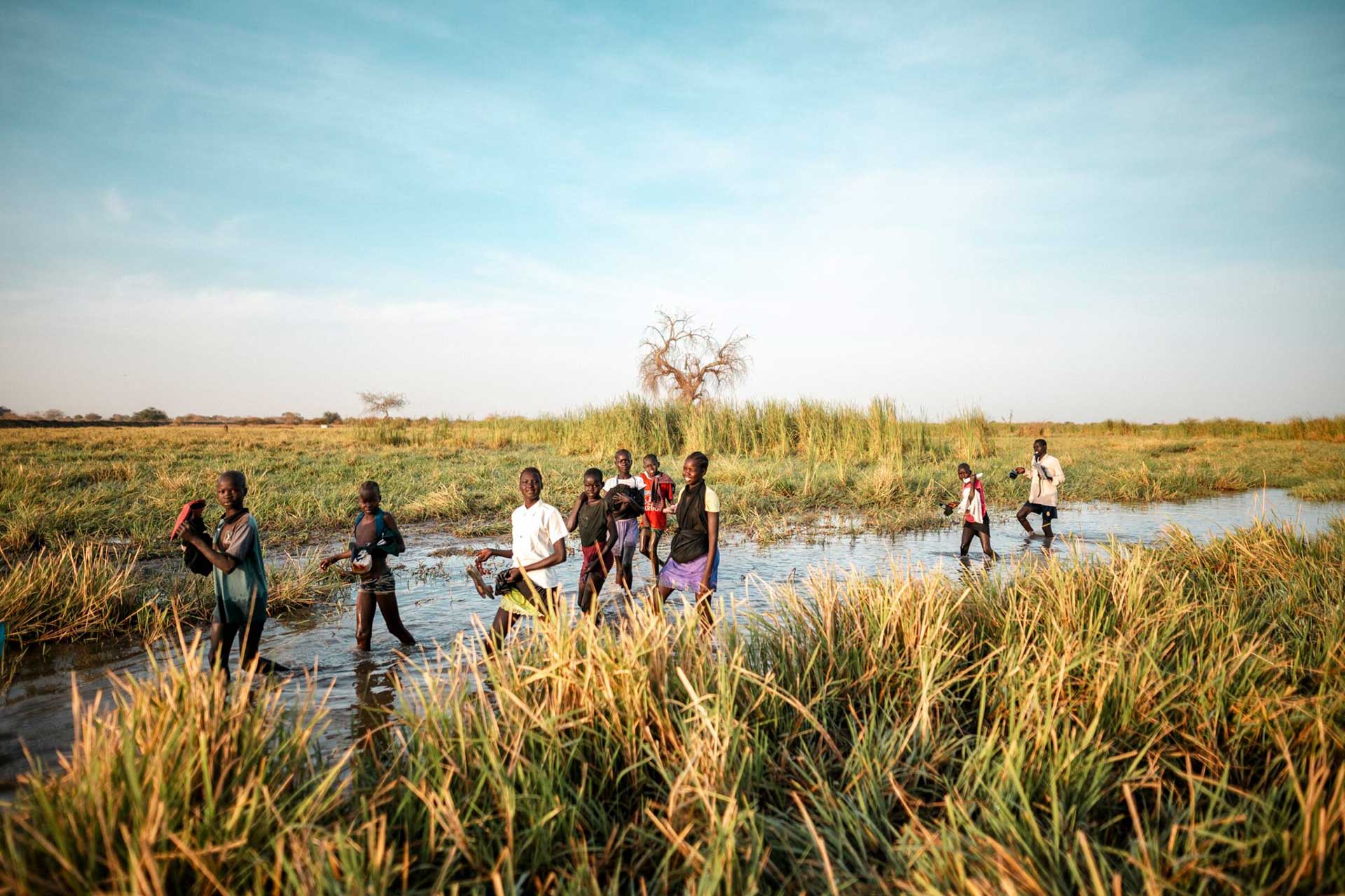 Joukko lapsia kävelee vetisessä suossa Etelä-Sudanissa kohti koulua.