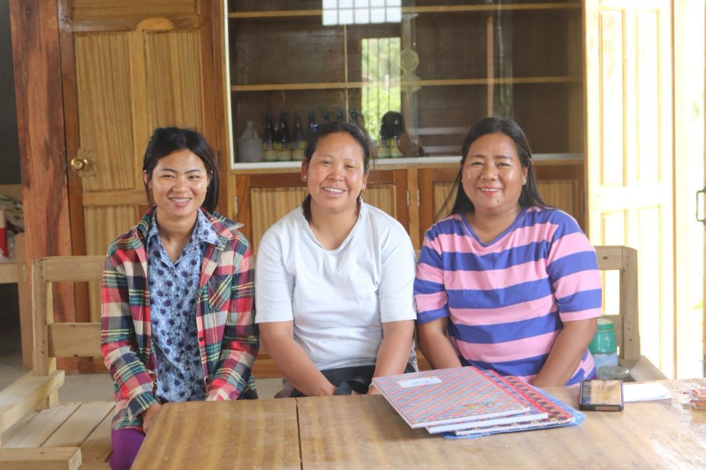 Three women sit at a table, smiling at the camera