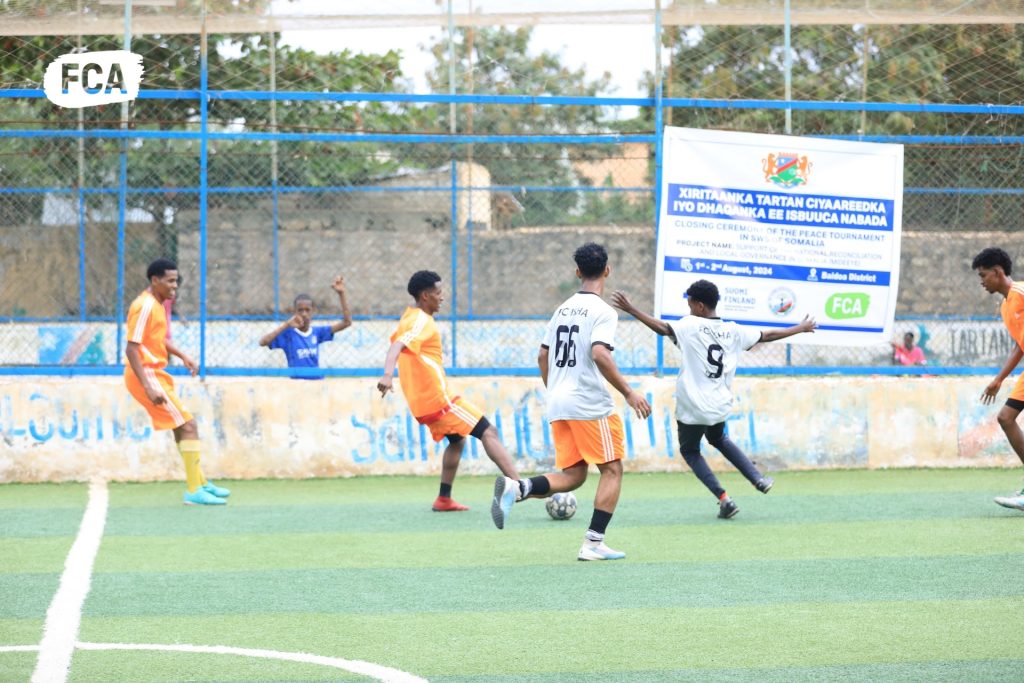 People playing football on a pitch. In the background we see a banner with FCA's logo.