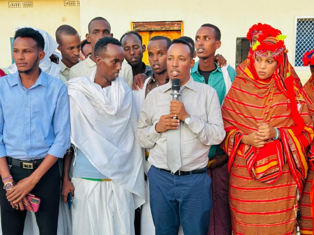 A man speaks into a microphone with men and women either side listening