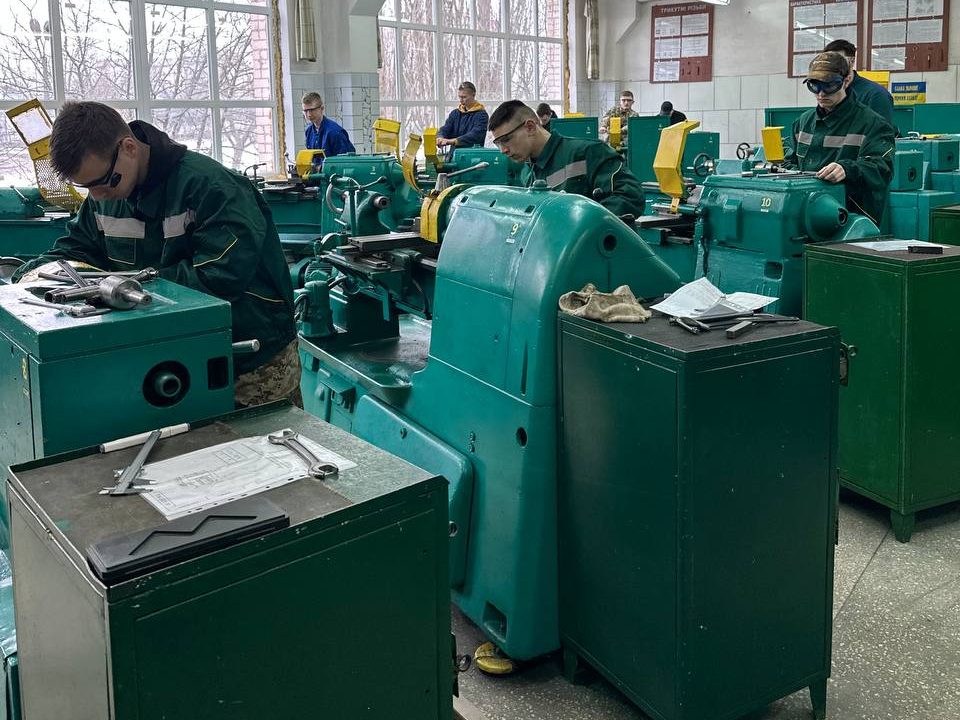 A workshop with a number of people working on mechanical lathes.