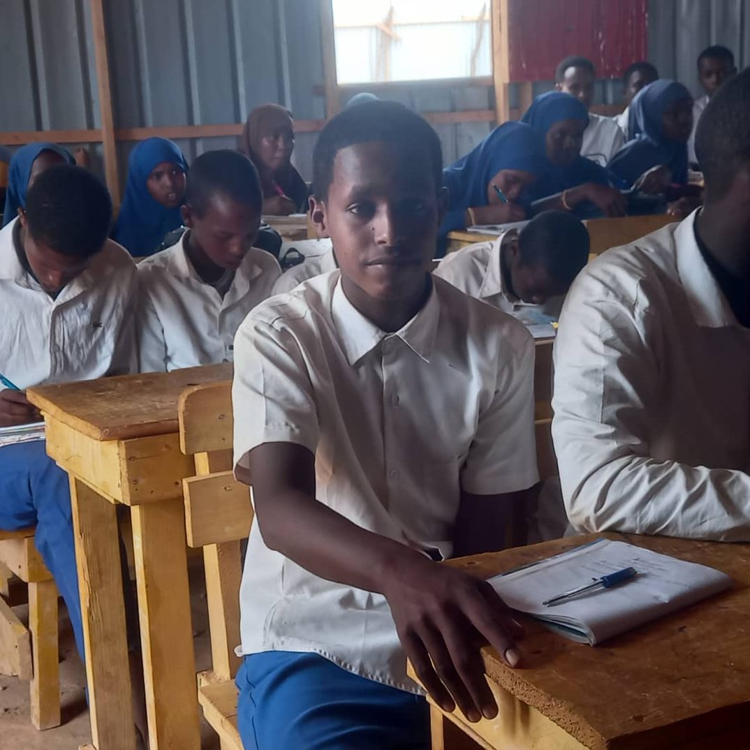 A boy in school uniform sits at a desk in a classroom.