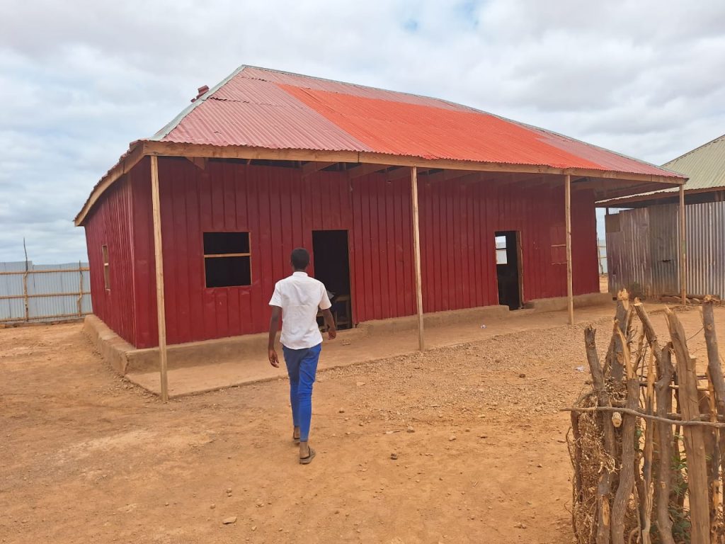 A schoolboy walks towards a large red building in a yard.