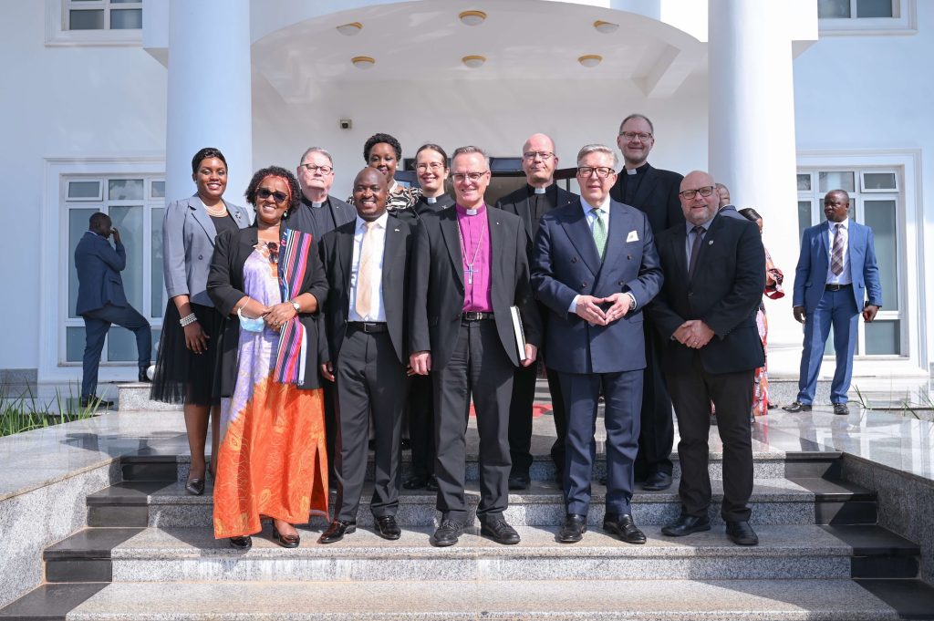 A group of people in business attire and wearing face masks pose for a photo on the steps of an official white building. Some of the people are wearing clerical collars