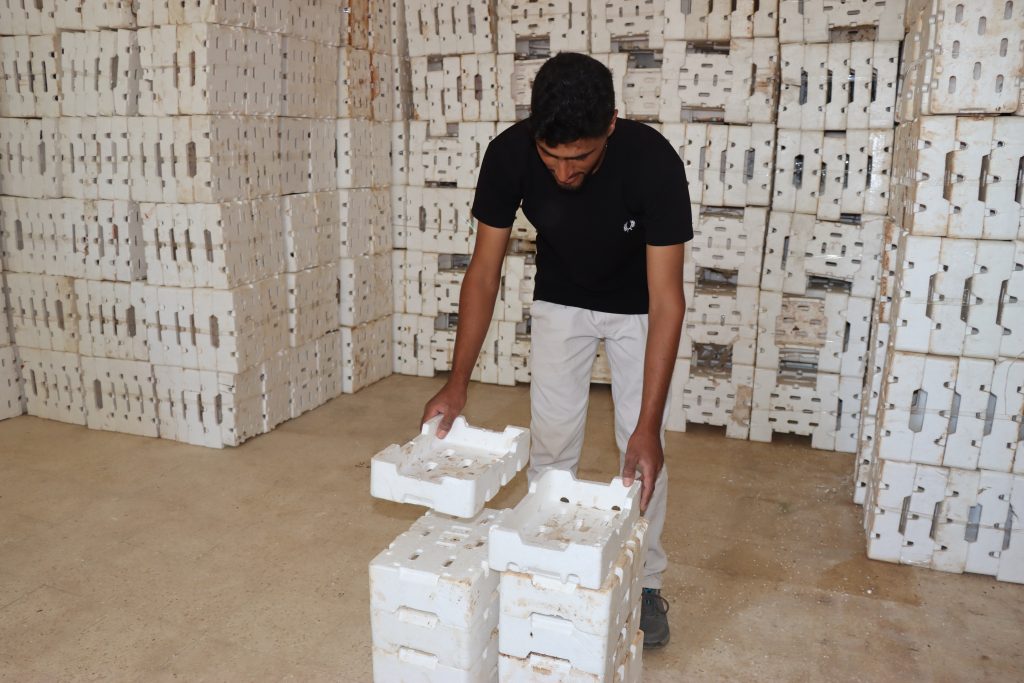 A man orders a pile of boxes in front of him. Behind him the same boxes are piled up to the ceiling.