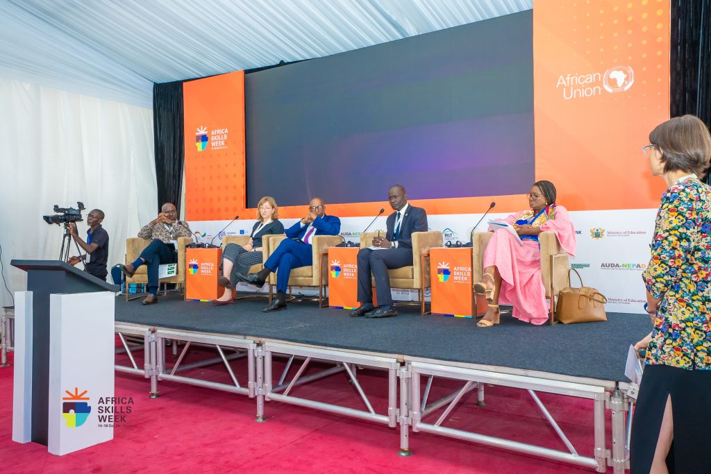 A number of people sitting in chairs on a stage. In the background are the logos of Africa Skills Week and the African Union