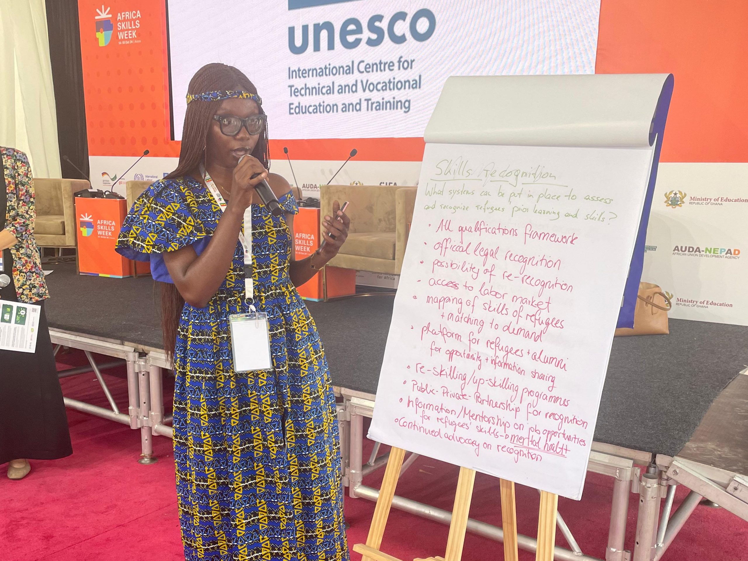 A woman stands by a flipchart and talks into a microphone