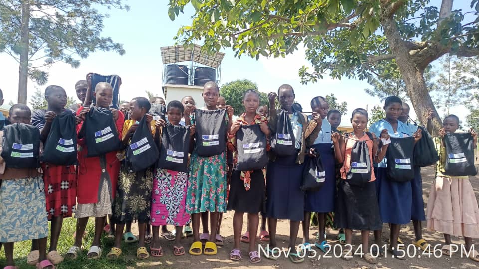 A group of girls in school uniform holding up bags with the FCA and EU logos on them