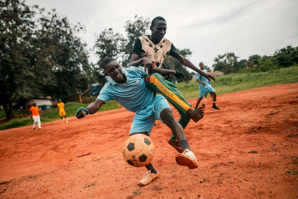 Kaksi nuorta miestä tavoittelee samaa jalkapalloa ja tönii samalla toisiaan Keski-Afrikan tasavallassa hiekkapohjaisella jalkapallokentällä. 