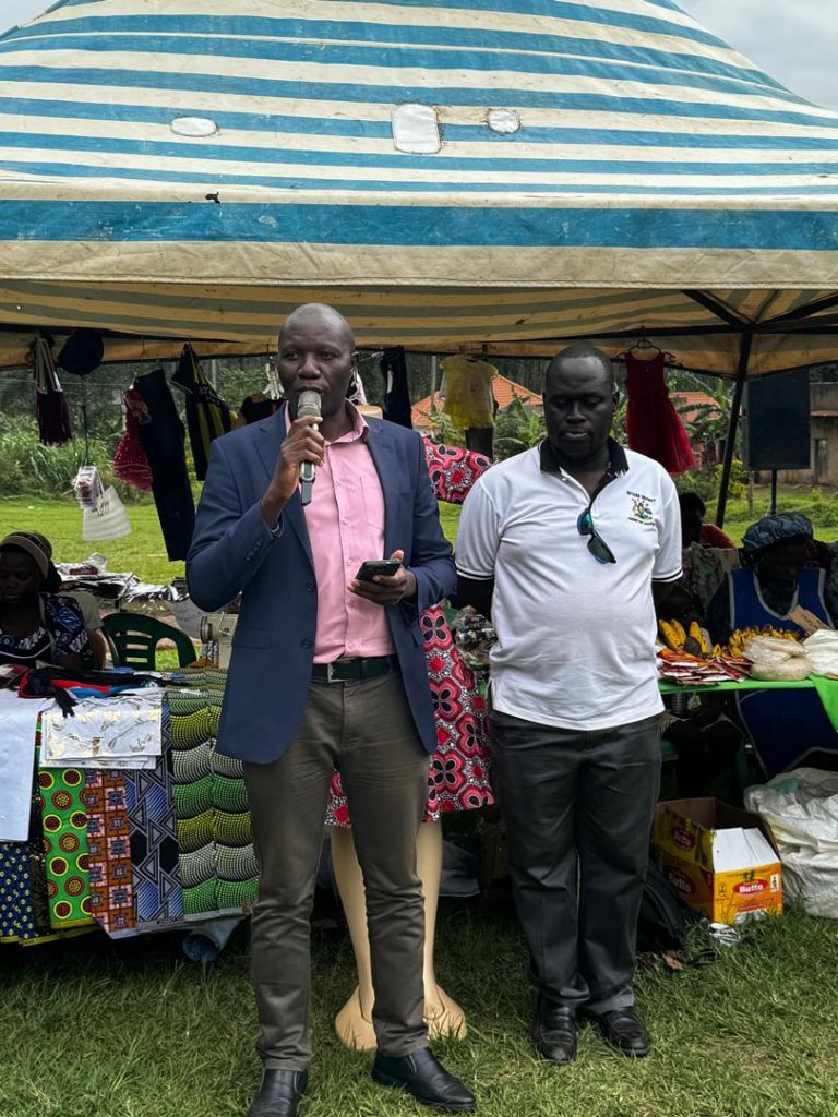 A man talking into a microphone at a market. Another man is standing next to him.