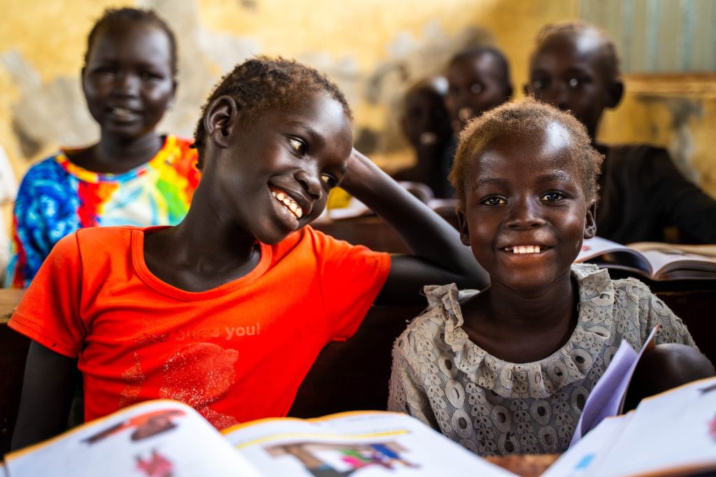 Two smiling girls sit at a school desk.