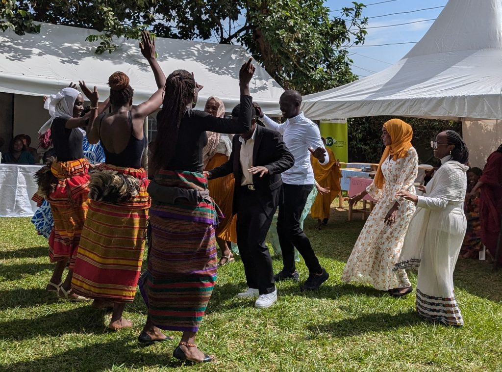 Men and women dance on a lawn outside. Marquees are in the background.