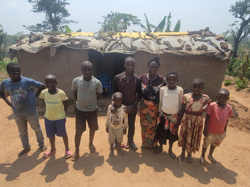 A mother and eight children standing in front of a mud hut