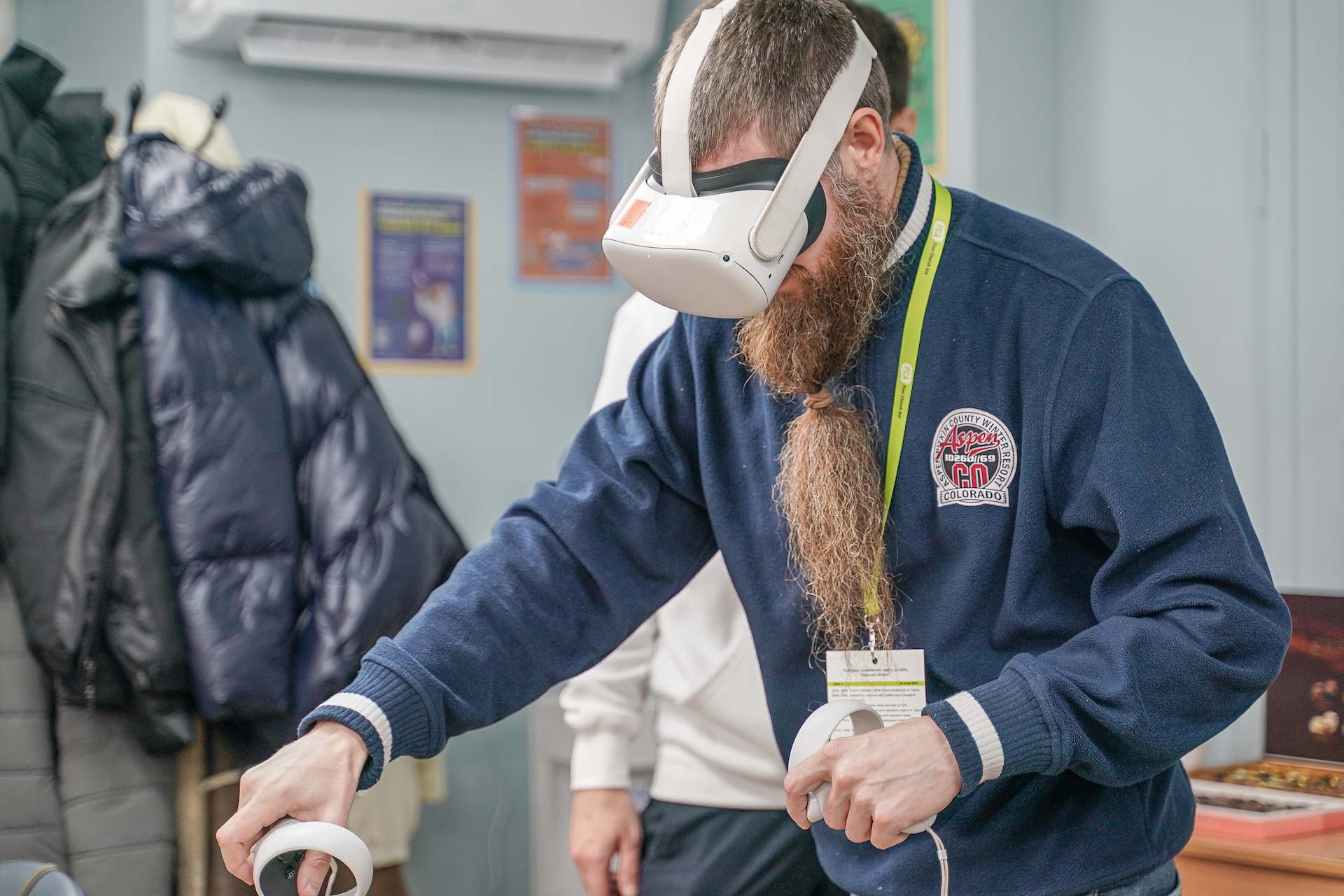 A mean is wearing a virtual reality (VR) headset and interacting with controllers in his hands. 