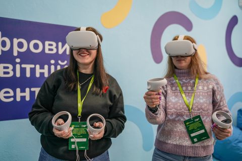 Two women wearing virtual reality (VR) headsets are smiling and holding controllers.