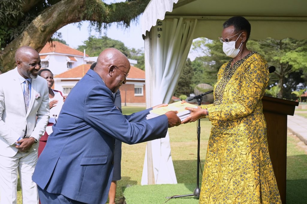 A man presents a report to a woman wearing a medical mask in an outside ceremony. Others around are smiling.