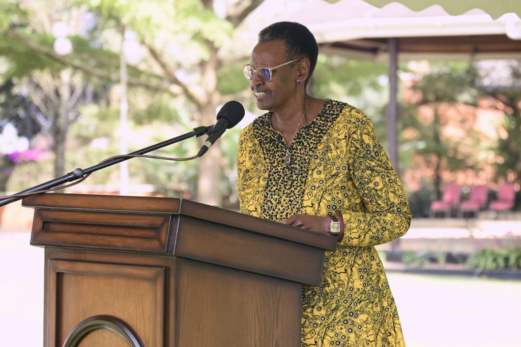 A woman in a patterned yellow dress gives a speech at a podium