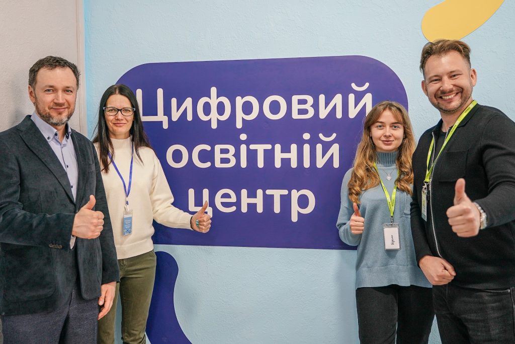 Four people stand in front of a sign saying