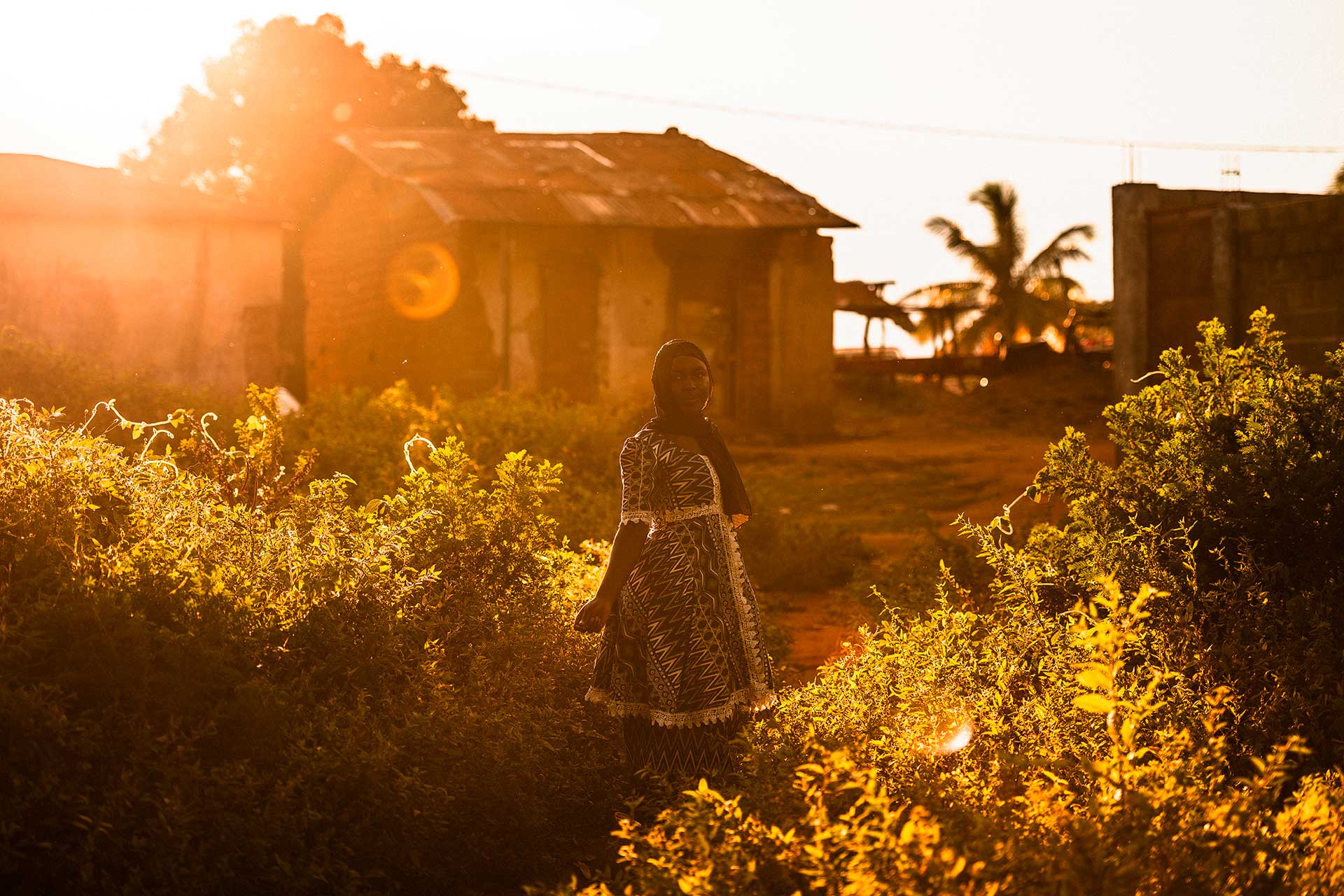 Nuori nainen seisoo auringonlaskun valaisemalla pihalla Keski-Afrikan tasavallassa. Taustalla näkyy rakennus.