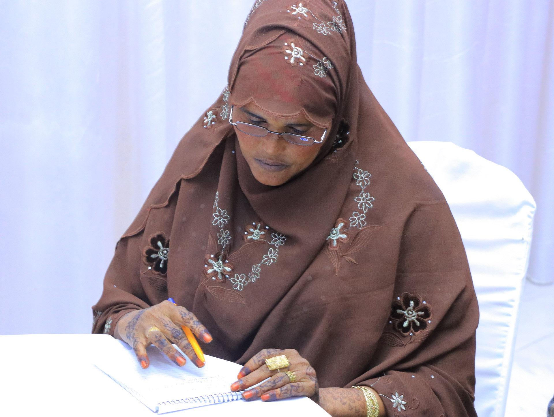 A woman in a brown patterned hijab sits at a table and studies her notes